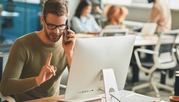 Copy space photo of calm brunette man holding index finger up while having a phonecall at his office desk